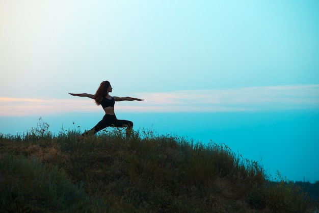 La silhouette della giovane donna sta praticando yoga