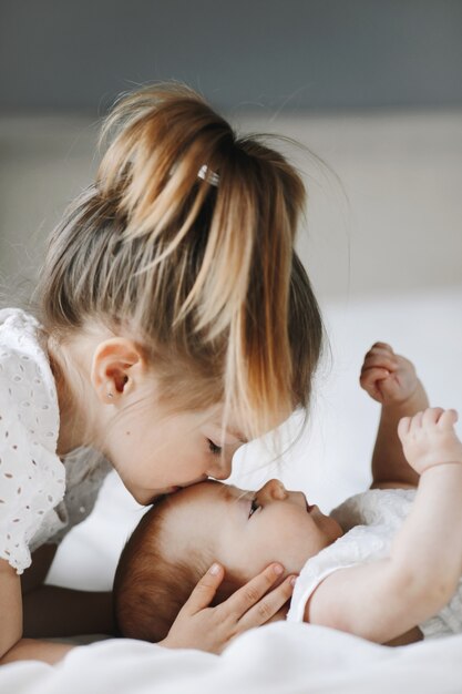 La sorella maggiore bacia la piccola bambina sulla fronte con gli occhi chiusi