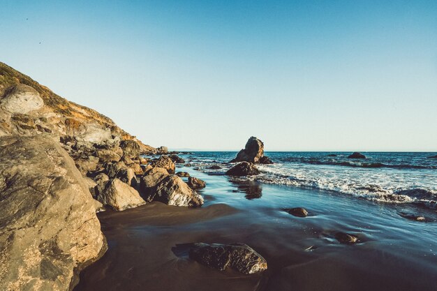 La spiaggia ondeggia colpendo la riva con le rocce un giorno soleggiato a Marin, la California