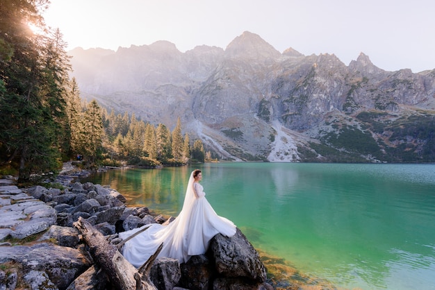 La sposa attraente sta stando vicino al lago dell'altopiano con la vista pittoresca delle montagne di autunno