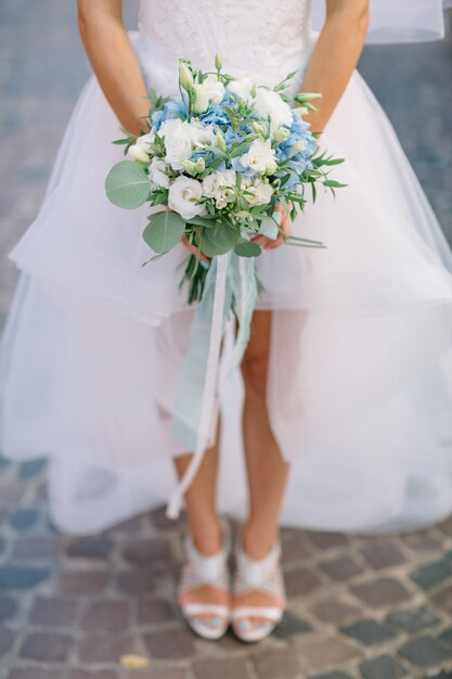 La sposa cammina sulla strada con il bouquet di nozze blu