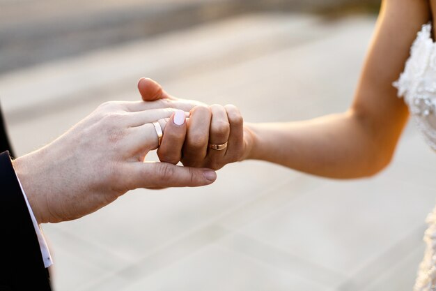 La sposa e lo sposo si tengono le mani con le fedi nuziali