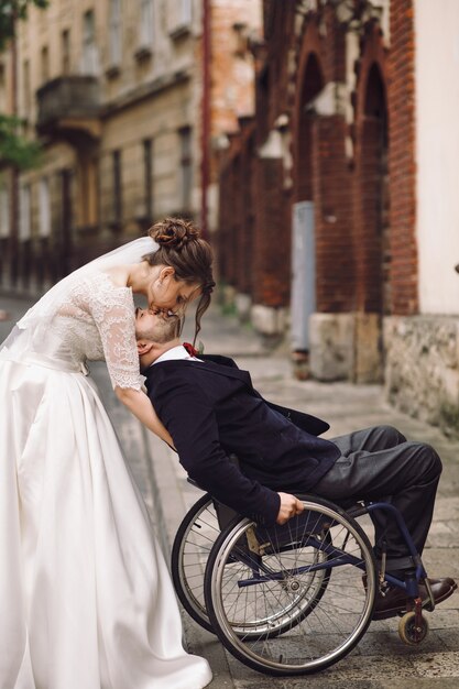 La sposa e lo sposo sulla sedia a rotelle posano sulla vecchia via europea