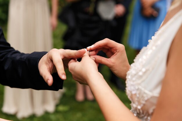 La sposa mette la fede nuziale sul dito dello sposo durante la cerimonia nel parco