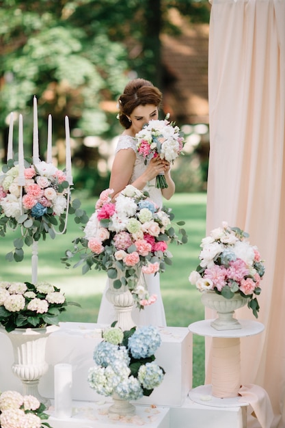 La sposa odora il bouquet di nozze in piedi davanti ai vasi da fiori