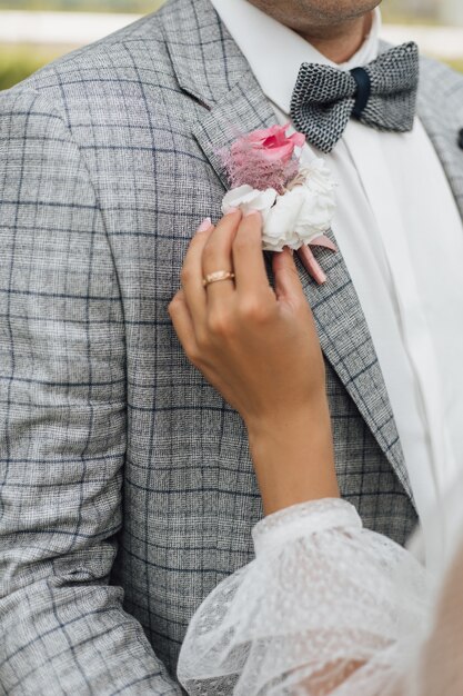 La sposa si aggrappa al boutonniere sulla giacca dello sposo, senza volto