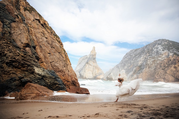 La sposa sta correndo sulla sabbia tra le rocce sulla spiaggia