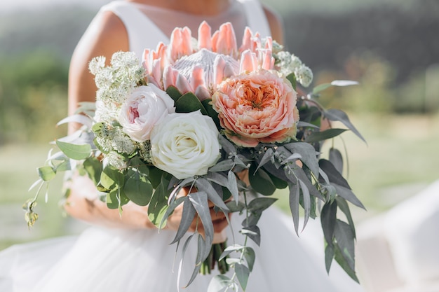 La sposa tiene il bellissimo bouquet da sposa con rose, eucalipto e protea gigante