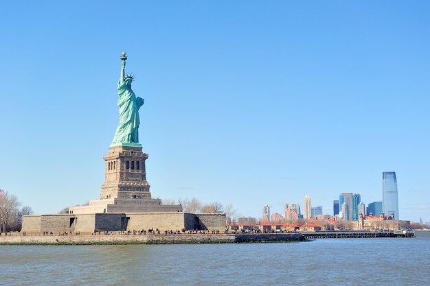 La Statua della Libertà si affaccia sullo skyline del centro di New York City Manhattan con grattacieli sul fiume Hudson con cielo blu chiaro.