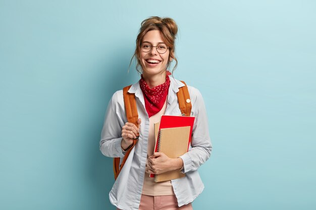 La studentessa positiva trasporta il blocco note a spirale, il taccuino, porta lo zaino, pronto per la scuola e le lezioni