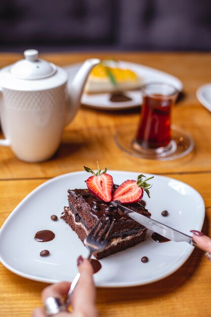 La torta al cioccolato con vista laterale con scaglie di cioccolato crema alla fragola aggiungono tè nero sul tavolo