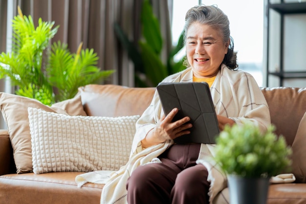 La vecchia nonna asiatica anziana si siede casualmente si rilassa la mano usa la tecnologia dello smartphone la videochiamata del dispositivo per avere il saluto e la conversazione con la sua famiglia il momento del periodo di quarantena dell'isolamento domestico bianco