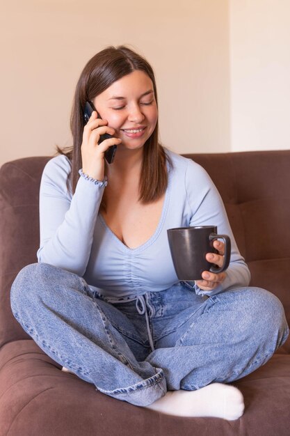 La vista completa della donna sorridente seduta a casa parla al telefono