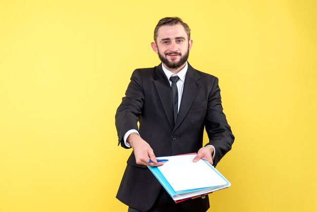 La vista frontale del giovane uomo d'affari con un sorriso indica con sicurezza con una penna i documenti per la firma su giallo