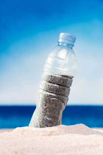 La vista frontale della bottiglia di plastica ha riempito di sabbia sulla spiaggia