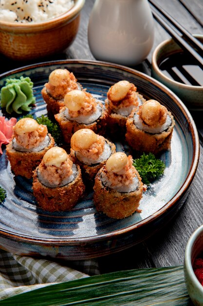 La vista laterale dei rotoli di sushi al forno con i gamberi lo zenzero e il wasabi su un piatto è servito con la salsa di soia su legno