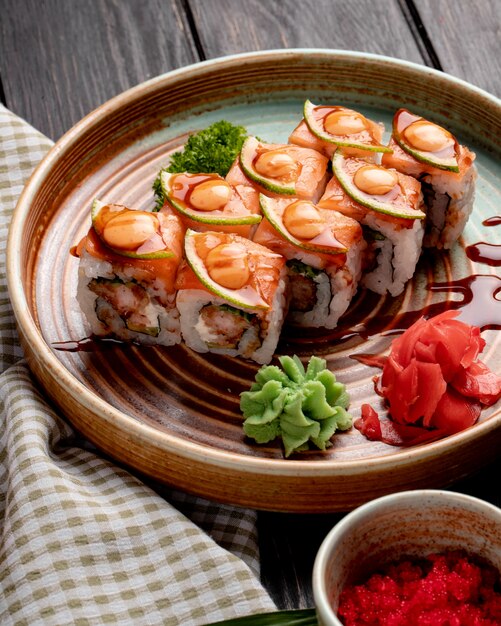 La vista laterale dei rotoli di sushi con i gamberi l'avocado e la crema di formaggio è servito con lo zenzero e il wasabi su un piatto su legno