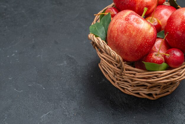 La vista laterale del primo piano fruttifica le mele e le ciliege appetitose nel cestino
