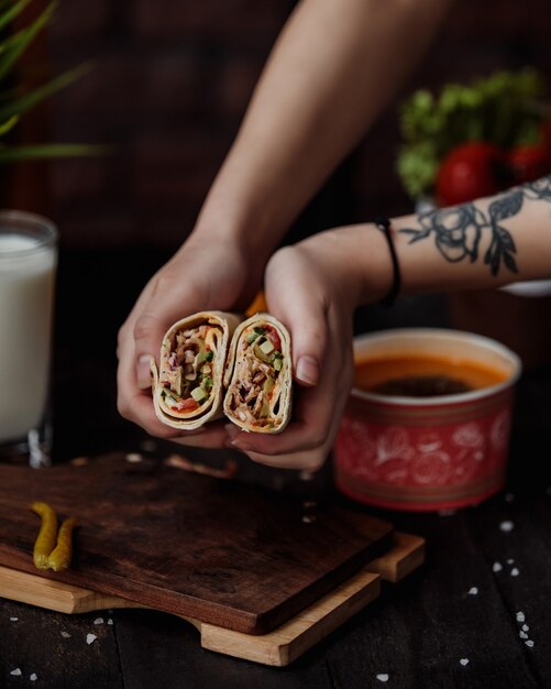 La vista laterale delle mani che tengono il doner ha riempito di sottaceti e salsa di verdure di pollo avvolti in lavash