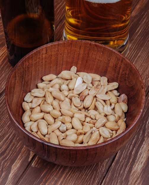 La vista laterale dello spuntino della birra ha salato le arachidi in una ciotola di legno con la tazza di birra su rustico