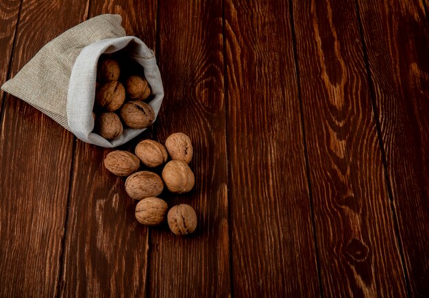 La vista laterale di intere noci ha sparso da un sacco su fondo di legno con lo spazio della copia