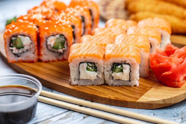 La vista laterale la California e Philadelphia rotola con la salsa di soia e lo zenzero del caviale di tobiko del salmone del formaggio cremoso su un bordo