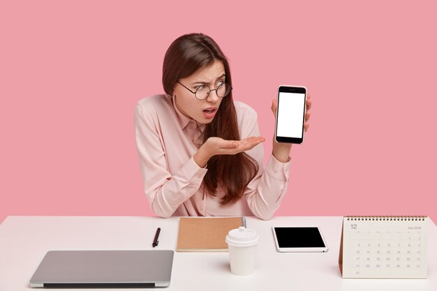 La vista orizzontale della donna frustrata dimostra qualcosa sullo schermo vuoto del telefono cellulare