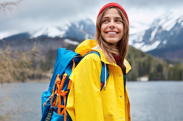 La vista orizzontale della turista femminile europea ottimista sembra felicemente da parte, ama camminare vicino al lago di montagna, ammira uno splendido scenario. Persone