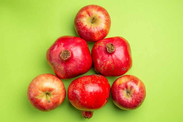 La vista ravvicinata dall'alto fruttifica i melograni appetitosi e tre mele rosse sulla superficie verde