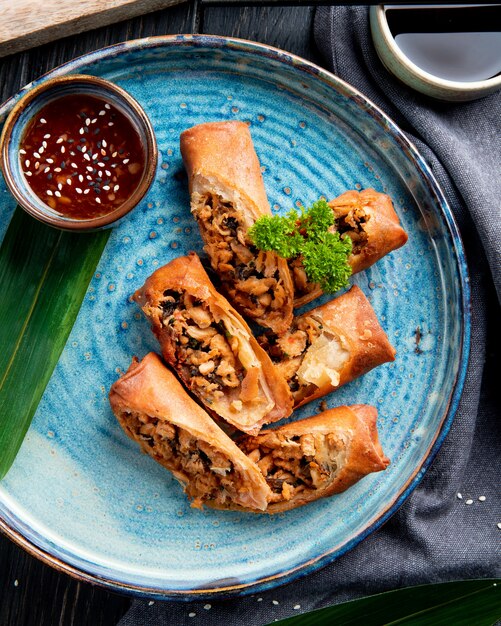 La vista superiore degli involtini primavera fritti con il pollo e le verdure è servito con la salsa di soia su un piatto sul nero