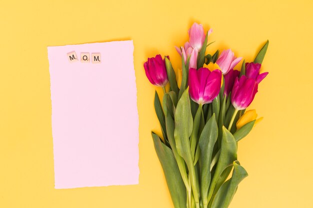 La vista superiore dei fiori del tulipano con la carta in bianco e la mamma mandano un sms a sui blocchi di legno sopra il contesto giallo