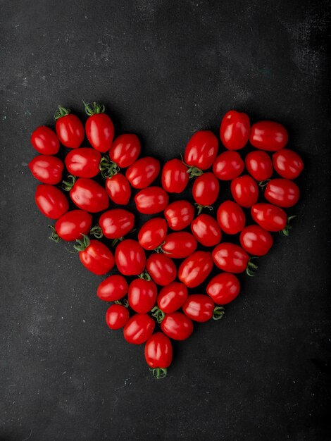 La vista superiore dei pomodori ciliegia freschi ha sistemato a forma di cuore su fondo nero