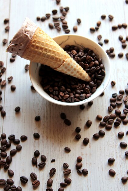 La vista superiore del cono di gelato in una ciotola ha riempito di chicchi di caffè su bianco