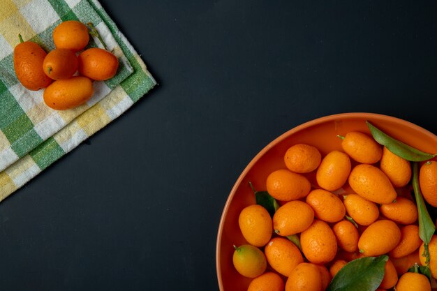 La vista superiore del kumquat maturo fresco fruttifica su un piatto sul nero con lo spazio della copia