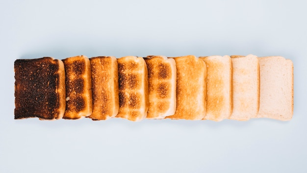 La vista superiore delle fette del pane alle fasi differenti della tostatura ha sistemato nella fila su fondo bianco