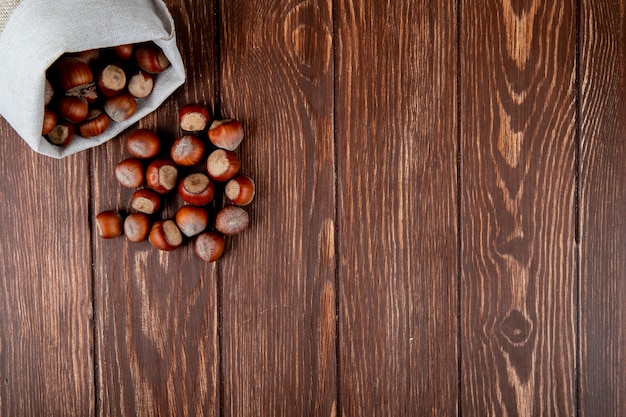 La vista superiore delle nocciole nelle coperture ha sparso da un sacco su fondo di legno con lo spazio della copia