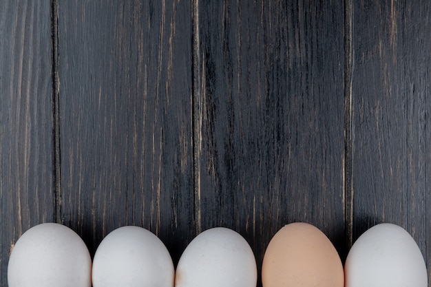 La vista superiore delle uova fresche e sane del pollo ha sistemato in una linea su un fondo di legno con lo spazio della copia