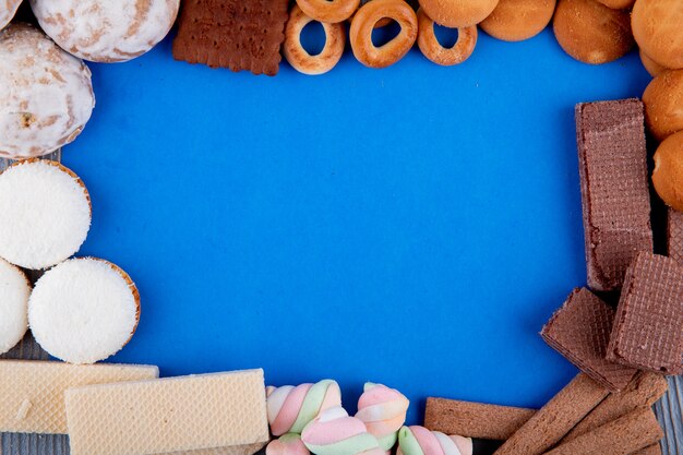 La vista superiore di vari tipi di caramelle gommosa e molle e di anelli di pane dolci dei biscotti ha sistemato in una forma del telaio su fondo blu con lo spazio della copia