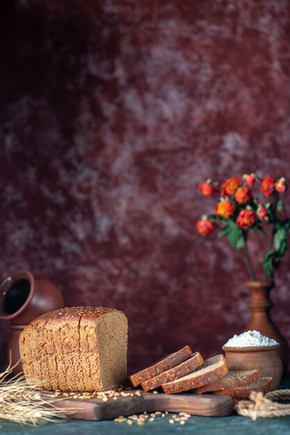 La vista verticale del pane nero dietetico picchia i grani sul tagliere di legno ciotole vaso di fiori su sfondo di colori misti marrone rossiccio