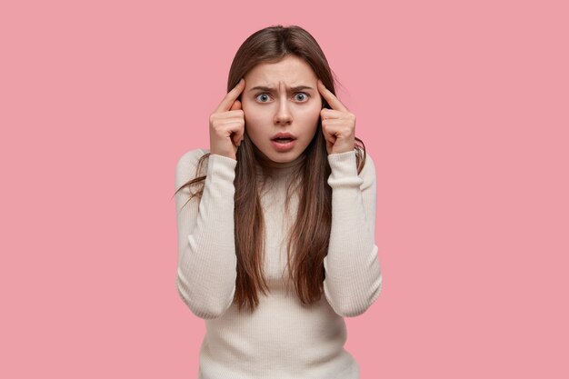 La vita in su di una donna dai capelli scuri insoddisfatta ha un'espressione del viso stupefatta, tiene gli indici sulle tempie, aggrotta la fronte, ha lunghi capelli neri