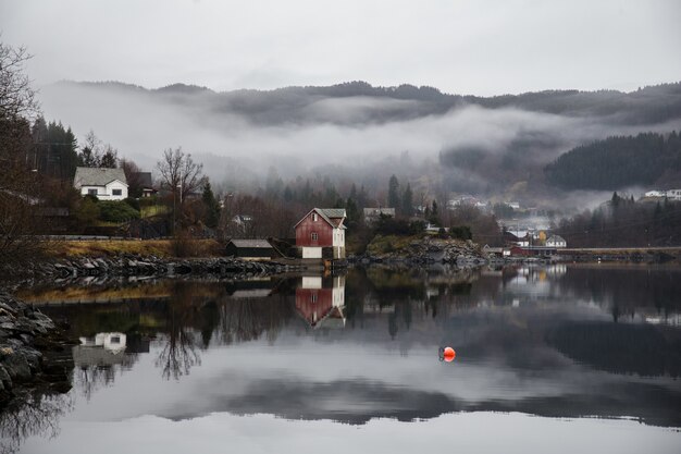 Lago circondato da edifici con montagne coperte di foreste e nebbia che si riflettono sull'acqua