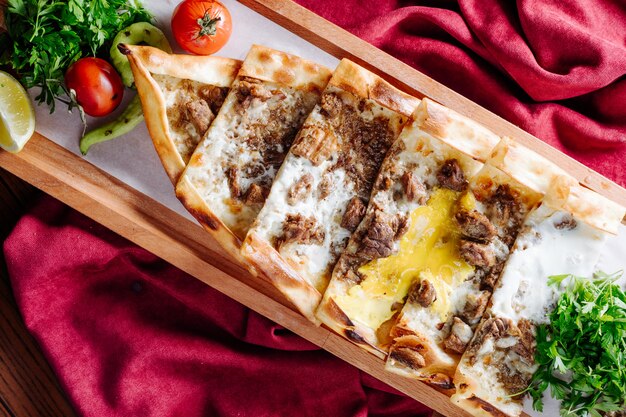 Lahmacun tradizionale turco con ripieno di carne e formaggio servito all'interno del piatto di legno.