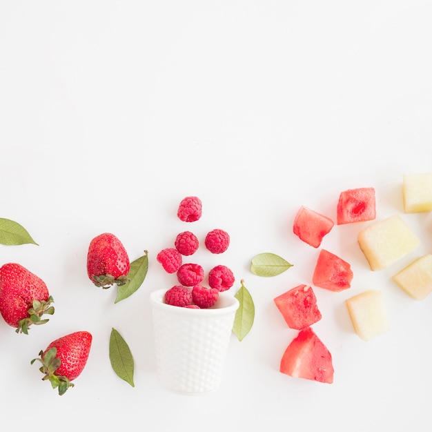 Lamponi freschi rovesciati davanti vetro con fragola; anguria e ananas isolato su sfondo bianco