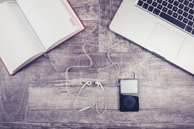 Laptop, notebook per la scrittura e lettore musicale dall'alto su uno sfondo di legno