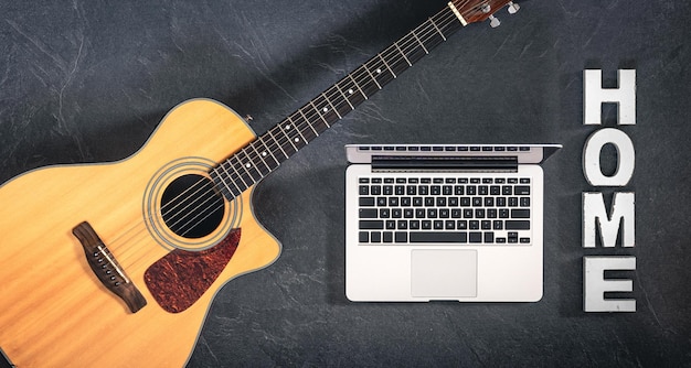 Laptop per chitarra acustica e parola decorativa a casa su uno sfondo scuro
