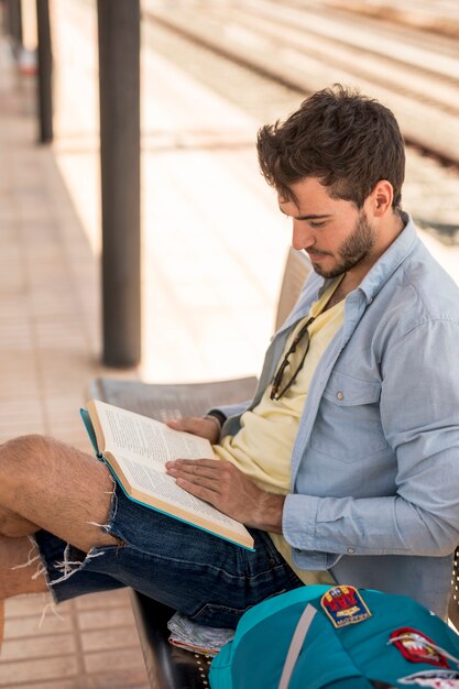 Lateralmente di un uomo che legge un libro sulla stazione ferroviaria