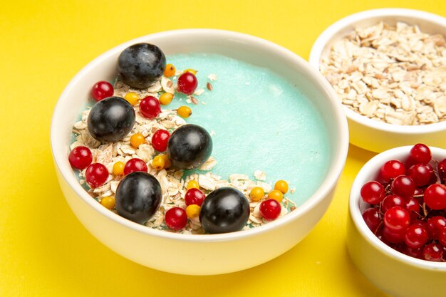 Lato vista ravvicinata bacche ciotole di appetitosi frutti di bosco colorati e farina d'avena sul tavolo giallo