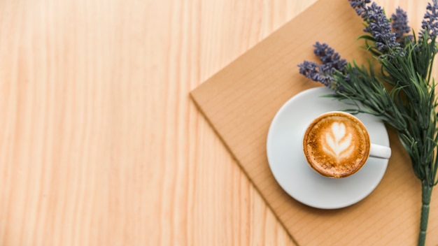 Latte del caffè, taccuino e fiore di lavanda sul contesto di legno