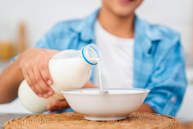 Latte di versamento del ragazzo del primo piano sopra i cereali