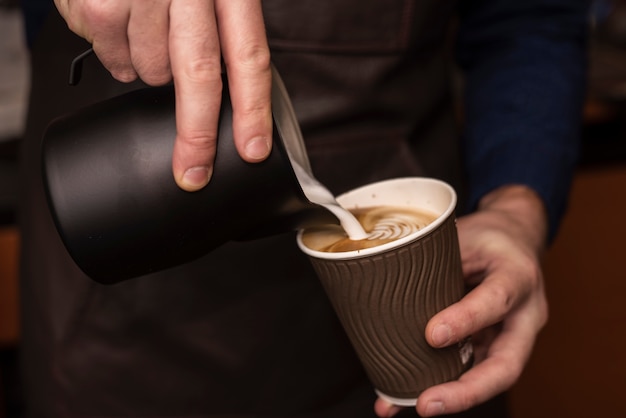 Latte di versamento della persona del primo piano nella tazza di caffè